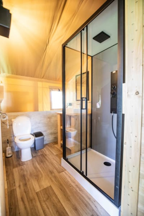 Baño moderno con ducha de vidrio y inodoro en una tienda safari en Camping Les Bouleaux, Francia.
