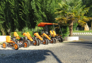 Verschillende oranje trapkarts en een familiefiets met zonnedak staan geparkeerd bij Camping la Salvinie, Frankrijk.