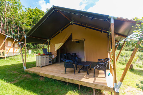 Safari tent met eigen terras, zitgedeelte en keukenblok op een groene, zonnige camping in de natuur.