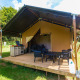 Safari-Zelt mit privater Terrasse und Sitzbereich auf einem sonnigen Campingplatz inmitten grüner Natur.
