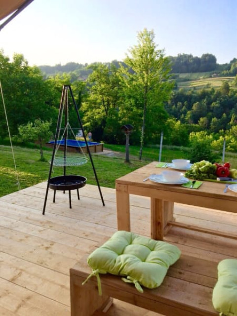 Holzterrasse mit Esstisch und Grill vor einer grünen Aussicht am Safari-Zeltplatz Camping Sretanwolf, Kroatien.
