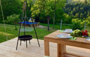 Holzterrasse mit Esstisch und Grill vor einer grünen Aussicht am Safari-Zeltplatz Camping Sretanwolf, Kroatien.