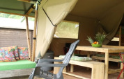 Tienda safari con muebles de madera y cojines coloridos en Camping Sretanwolf, Croacia, parcialmente abierta.