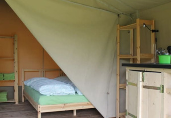 Interior of a safari tent at Camping Sretanwolf, Croatia, with bed, shelves, wooden furniture, and striped rug.