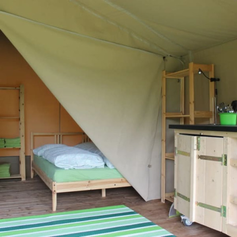 Interno di una tenda safari al Camping Sretanwolf in Croazia, con letto, scaffali e tappeto a righe verdi.