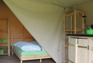 Interior de una tienda safari en Camping Sretanwolf, Croacia, con cama, estantes, alfombra y muebles de madera.