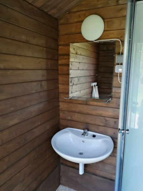 Lavabo con espejo y lámpara en un baño revestido de madera en Safari tent + sanitary en Camping Sretanwolf, Croacia.