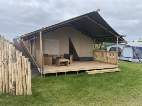 Tienda safari con baño en Camping Jagtveld en Países Bajos, con porche de madera y área para sentarse.