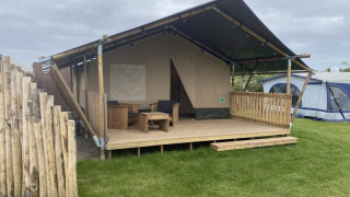 Safari-Zelt mit Toilette auf Camping Jagtveld in den Niederlanden, mit Holzterrasse und Sitzbereich.