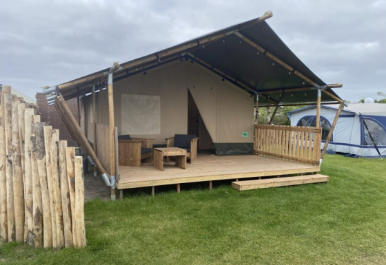 Safaritent met eigen toilet op Camping Jagtveld in Nederland, met houten veranda en zithoek buiten.