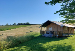 Safari tent with porch and sanitary at Tenuta Tredici Ulivi, Italy, surrounded by fields and blue sky.