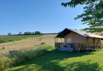 Tienda safari con porche y sanitario en Tenuta Tredici Ulivi, Italia, rodeada de campo y cielo azul.