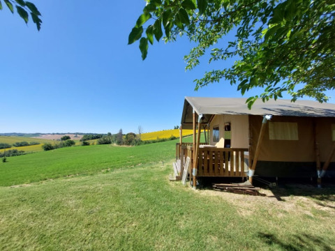 Safari tent with a wooden porch overlooking green fields at Tenuta Tredici Ulivi in Italy under blue sky.