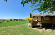 Safari tent with a wooden porch overlooking green fields at Tenuta Tredici Ulivi in Italy under blue sky.