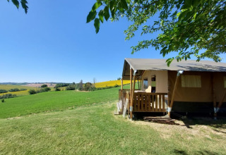 Tienda safari con porche de madera y vistas a campos verdes en Tenuta Tredici Ulivi, Italia, bajo cielo azul.
