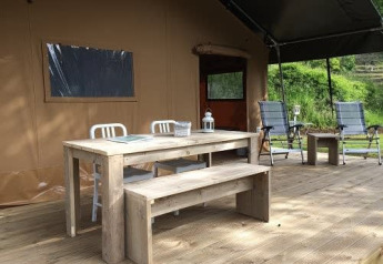 Terrasse extérieure d'une tente safari avec table, banc et chaises en bois à Tenuta Tredici Ulivi, Italie.