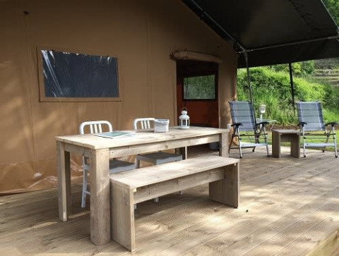 Outdoor deck of a safari tent featuring a wooden dining table, bench, and chairs at Tenuta Tredici Ulivi, Italy.