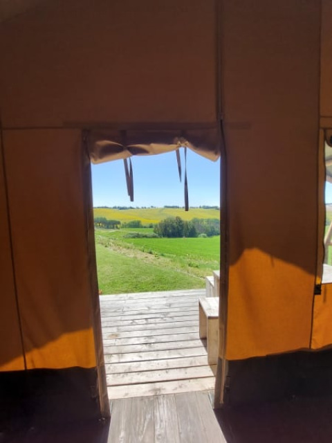 Blick aus einem Safarizelt mit Sanitäranlagen in Tenuta Tredici Ulivi, Italien, auf grüne Felder.