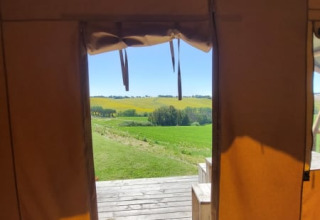 View from a safari tent with ensuite at Tenuta Tredici Ulivi, Italy, looking out onto lush green fields.