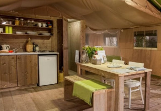 Innenraum eines Safarizelts mit Holzmöbeln, Küche und Esstisch bei Tenuta Tredici Ulivi, Italien.