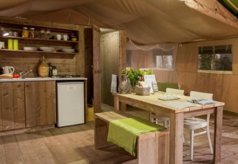 Innenraum eines Safarizelts mit Holzmöbeln, Küche und Esstisch bei Tenuta Tredici Ulivi, Italien.