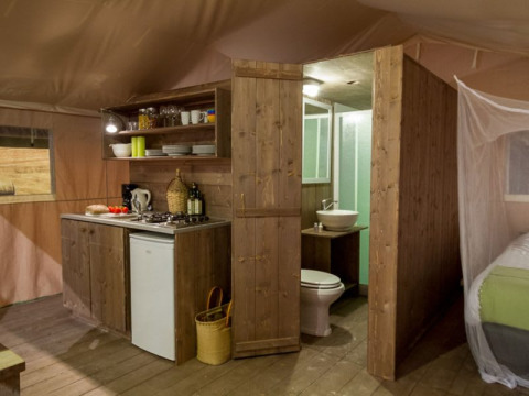 Interior view of a safari tent featuring a kitchen, bathroom, and bed at Tenuta Tredici Ulivi in Italy.