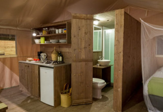 Interior view of a safari tent featuring a kitchen, bathroom, and bed at Tenuta Tredici Ulivi in Italy.