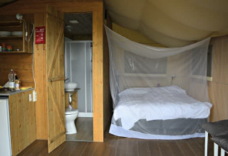 Interior de una tienda safari con cama, mosquitera, baño y pequeña cocina en Tenuta Tredici Ulivi, Italia.