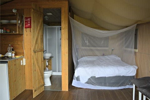 Interior de una tienda safari con cama, mosquitera, baño y pequeña cocina en Tenuta Tredici Ulivi, Italia.