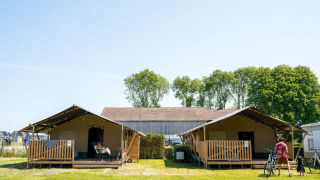 Dos tiendas safari con porches y visitantes en Camping Tussen de Diepen en los Países Bajos, día soleado.