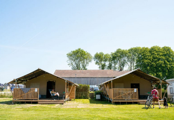 Dos tiendas safari con porches y visitantes en Camping Tussen de Diepen en los Países Bajos, día soleado.