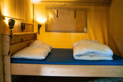 Indretning af en seng i et safari telt med træpaneler og blød belysning på Camping Tussen de Diepen.