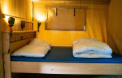 Interior de una tienda safari con cama de madera e iluminación suave en Camping Tussen de Diepen, Países Bajos.