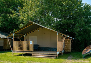 Tienda safari con terraza y servicios sanitarios en Camping Tussen de Diepen, Países Bajos, rodeada de árboles.