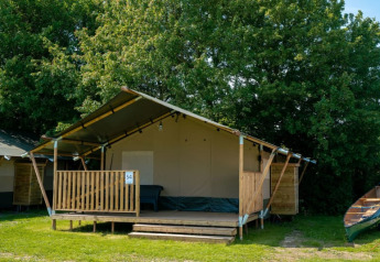 Tente safari avec terrasse et sanitaires au Camping Tussen de Diepen, Pays-Bas, entourée d’arbres.