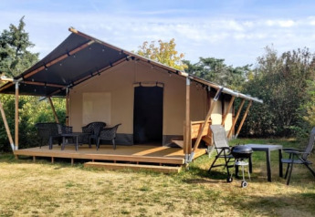 Tenda safari al Ballum Camping in Danimarca con veranda, sedie e barbecue immersi nella natura.