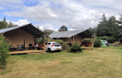 Dos tiendas de glamping de lujo y un coche en un entorno natural verde y tranquilo rodeado de árboles.