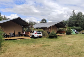 Dos tiendas de glamping de lujo y un coche en un entorno natural verde y tranquilo rodeado de árboles.
