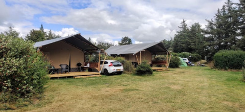 Zwei luxuriöse Glamping-Zelte und ein Auto inmitten einer grünen, bewaldeten Landschaft am Campingplatz.