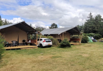 Dos tiendas de glamping de lujo y un coche en un entorno natural verde y tranquilo rodeado de árboles.