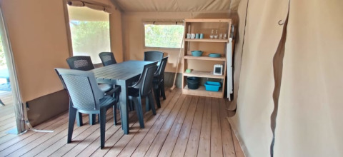 Safari-Zelt-Innenraum mit Esstisch, sechs schwarzen Stühlen und Regal mit Geschirr und Küchenutensilien.