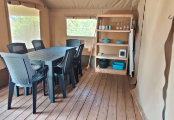 Intérieur de tente safari avec table à manger, six chaises noires et étagère en bois avec vaisselle.