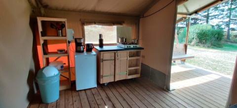 Área de cocina interior en una tienda glamping con suelo de madera, estufa, nevera y vista exterior.