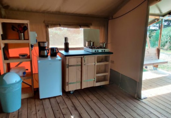 Zona cucina interna in una tenda glamping con pavimento in legno, fornello, mini-frigo e vista esterna.