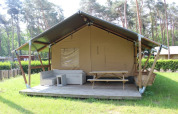 Tienda safari con terraza, asientos y mesa de picnic en Familiepark Goolderheide, Bélgica, rodeada de árboles.