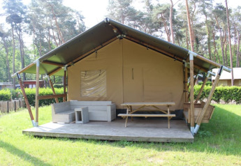 Tienda safari con terraza, asientos y mesa de picnic en Familiepark Goolderheide, Bélgica, rodeada de árboles.