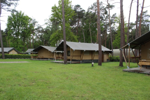 Tiendas safari con instalaciones sanitarias en Familiepark Goolderheide, Bélgica, rodeadas de árboles verdes.