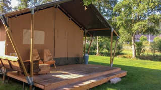 Tienda de safari con terraza de madera y sillas, situada en un césped verde rodeado de árboles.