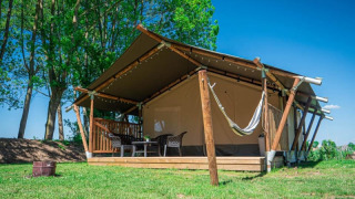 Safari-Zelt mit Sanitäranlage auf Camping de Tolbrug in den Niederlanden, umgeben von Bäumen und Gras.