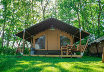 Vista esterna della Lodge Compact al Camping de Tolbrug nei Paesi Bassi, circondata da alberi e prato verde.